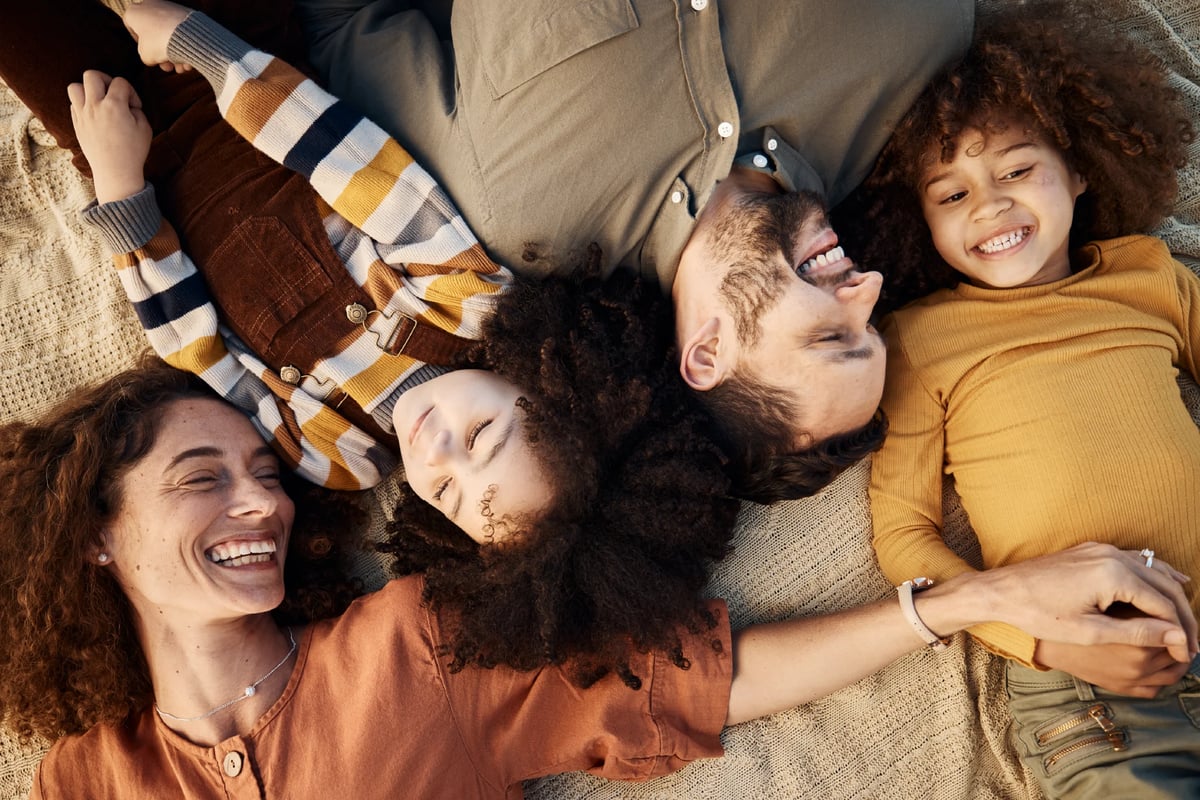 Happy family of four lying together on a blanket, smiling and bonding outdoors in warm earth-toned clothing