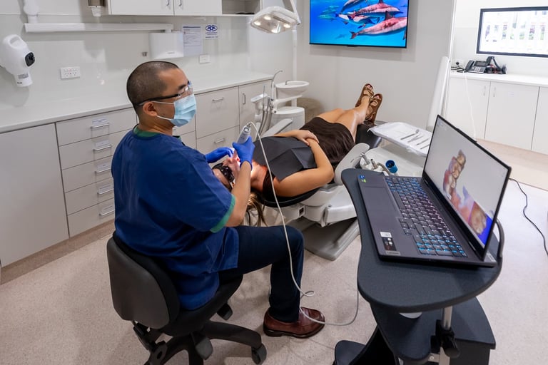 Dentist in blue shirt and mask examining patients teeth in modern dental office with equipment and monitors visible