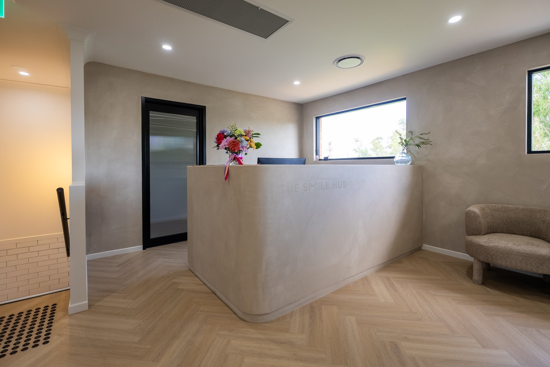 Modern reception desk with white counter in bright office lobby featuring herringbone wood flooring and minimalist decor