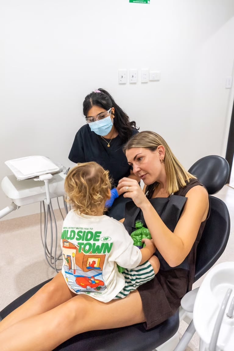Pediatric dentist examining a young child in dental office while masked assistant observes