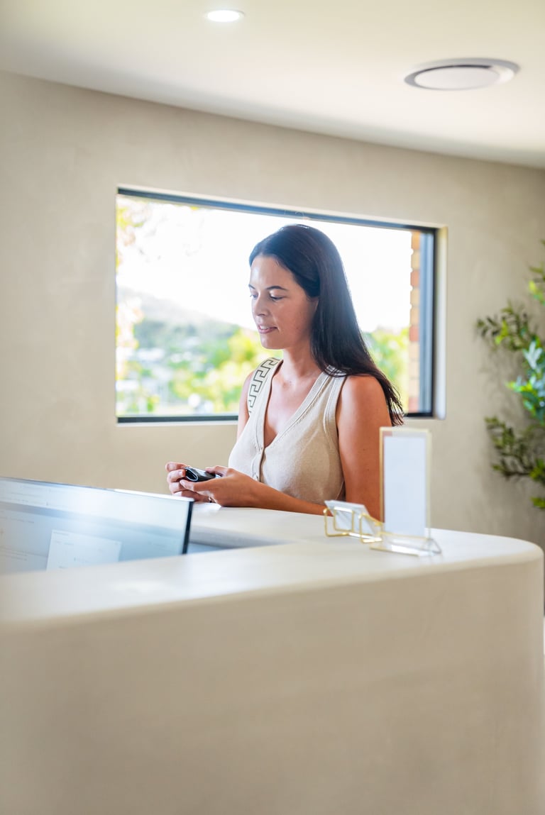 Woman at modern reception desk holding phone, looking out large window with scenic outdoor view