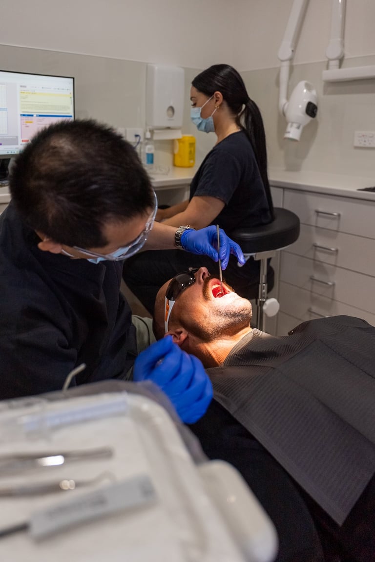 Dentist examining patients teeth in a clinical setting with dental equipment visible in background