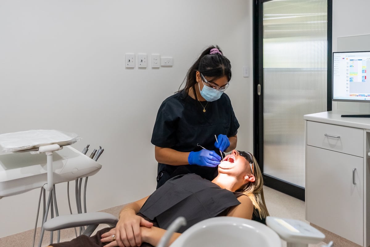 Dentist in mask and gloves examining patient in dental chair in modern clinic office