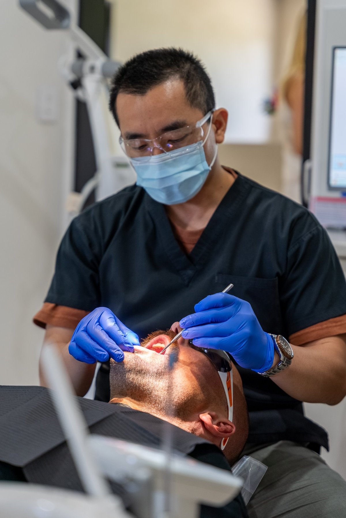 Dentist in mask and blue gloves examining patients teeth in a clinical setting