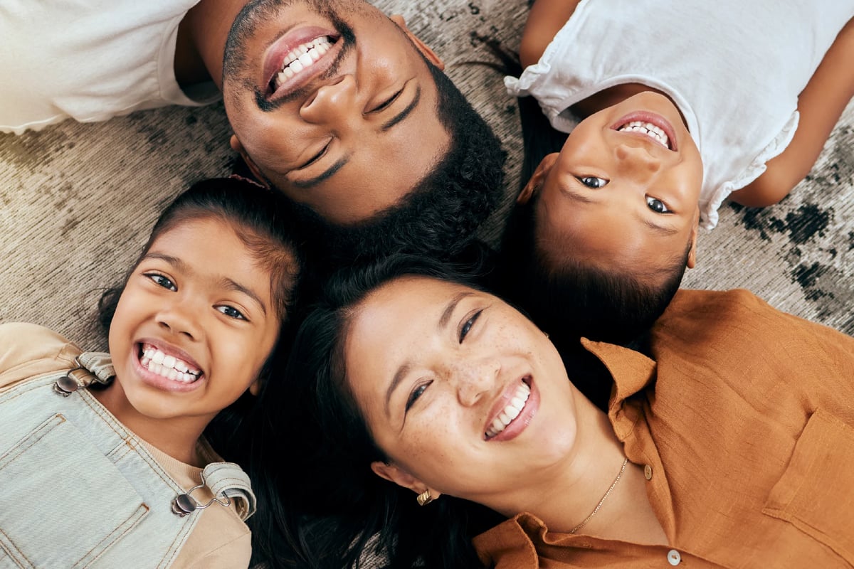 Happy family of five lying on a bed together, smiling and looking down at the camera in a playful overhead shot